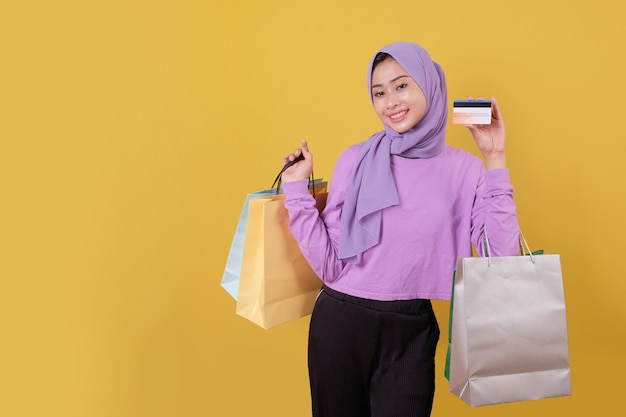 Sourire heureuse jolie fille utilisant une carte de crédit pour gaspiller de l'argent dans un centre commercial, tenant des sacs à provisions, acheter des cadeaux ou des cadeaux, offrez-vous la journée