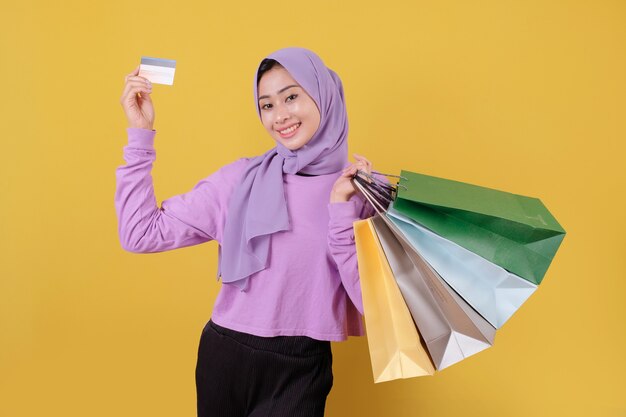 Sourire heureuse jolie fille utilisant une carte de crédit pour gaspiller de l'argent dans un centre commercial, tenant des sacs à provisions, acheter des cadeaux ou des cadeaux, offrez-vous la journée