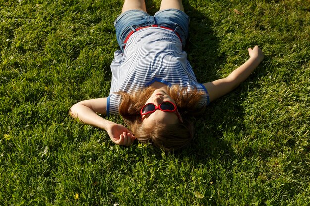 Sourire heureux belle et jeune fille s'étendant sur le temps dans le parc de la ville Lunettes de soleil coeurs rouges