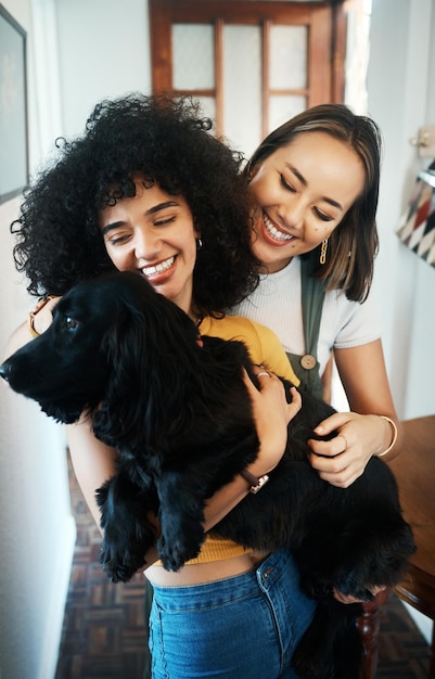 Sourire heureux et couple lesbien tenant un chien dans un appartement moderne pour créer des liens Ensemble Famille d'amour et jeunes femmes lgbtq interraciales embrassant et embrassant leur doux chiot animal de compagnie à la maison