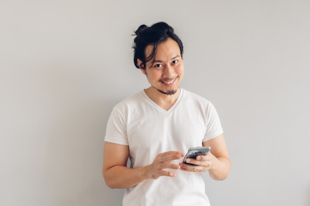 Sourire et heureux homme aux cheveux longs en tshirt occasionnel blanc utilise un smartphone