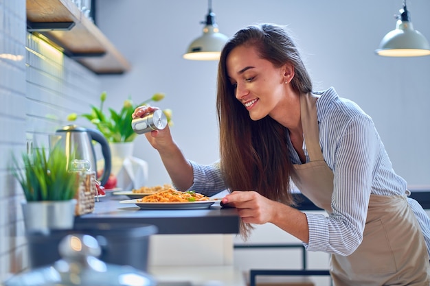 Sourire heureux joyeux mignon femme cuisine femme au foyer sel et prépare un plat pour le dîner