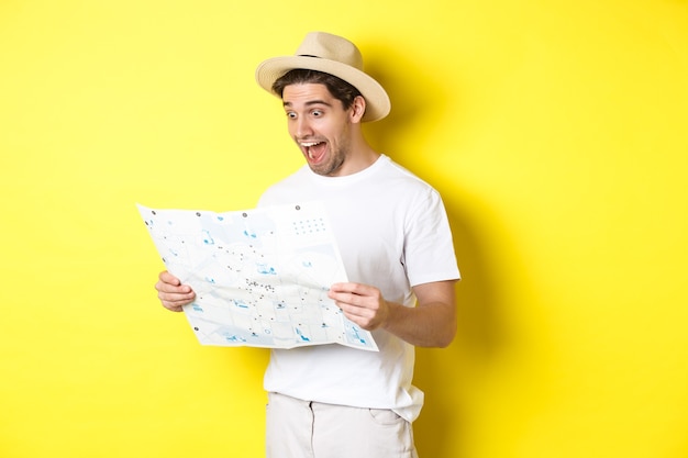 Sourire heureux touriste regardant la carte avec des sites touristiques, debout contre le mur jaune
