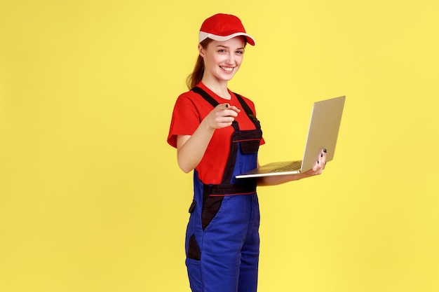 Sourire heureux travailleur femme travaillant en ligne sur un ordinateur portable à la recherche et pointant vers la caméra