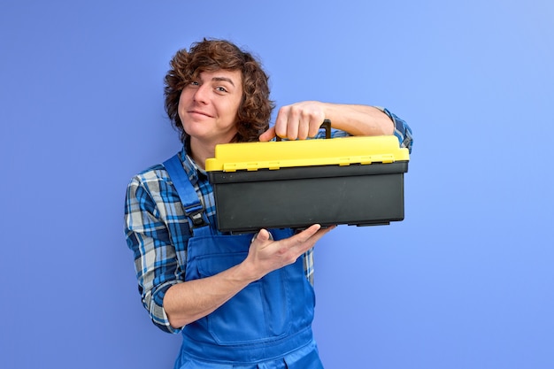Sourire homme caucasien en combinaison ouvrant boîte à outils isolé sur mur bleu studio