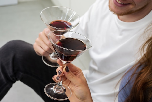 Sourire homme et femme assis sur le sol de la cuisine et tinter des verres de cocktails. Amant de couple, passer du temps ensemble, s'amuser et boire à la maison.