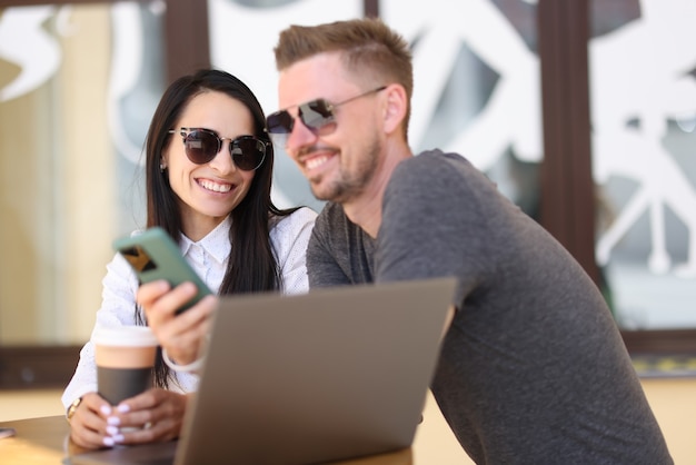 Sourire homme et femme à lunettes de soleil communiquent dans le café près d'un ordinateur portable
