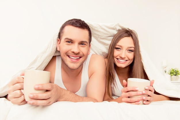 Sourire homme et femme se prélassant avec une couverture et du thé chaud