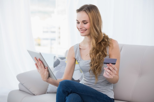 Sourire jeune femme assise sur un canapé avec tablette pour faire du shopping en ligne