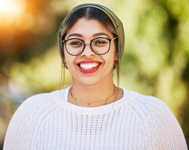 Sourire de jeune femme et portrait heureux en plein air dans la nature avec des lunettes et un sourire éclatant en été Style de mode et modèle féminin de la génération z ou étudiant avec un foulard turban bonheur et état d'esprit positif