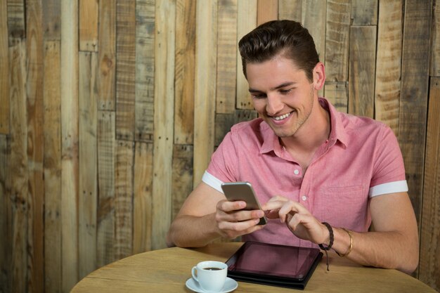 Sourire jeune homme à l'aide de téléphone intelligent à table dans un café