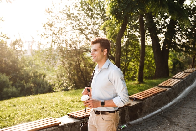 Sourire jeune homme en chemise marchant dans le parc de la ville