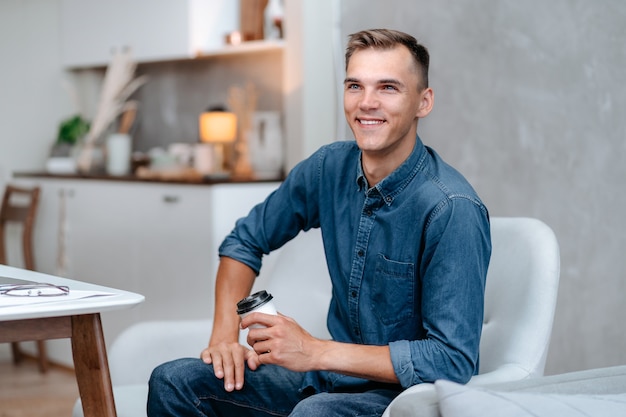 Sourire jeune homme avec une tasse de café assis sur une chaise