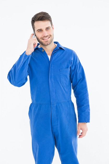 Sourire jeune mécanicien mâle à l&#39;aide de téléphone portable sur fond blanc