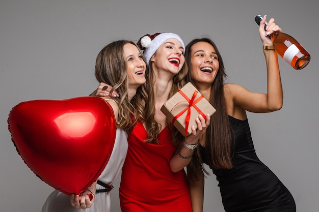 Sourire de jolies amies vont célébrer ensemble tout en tenant un ballon en forme de coeur et une boîte-cadeau, champagne.