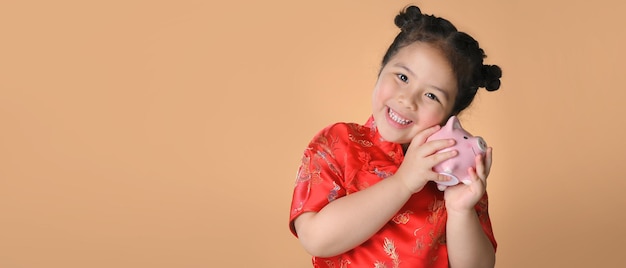 Sourire de jolies filles asiatiques en robe traditionnelle chinoise rouge tenant une tirelire rose. Concept de joyeux nouvel an chinois.