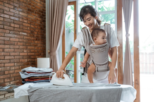 Sourire Joyeuse Femme Asiatique Repasser Le Linge Tout En Tenant Sa Petite Fille