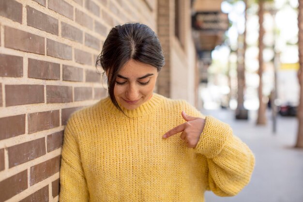 Sourire joyeusement et avec désinvolture en regardant vers le bas et en pointant vers la poitrine