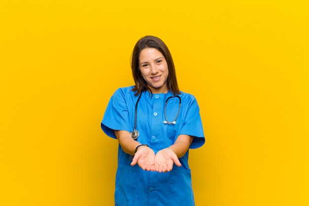 Sourire joyeusement avec un regard amical, confiant et positif, offrant et montrant un objet ou un concept isolé contre un mur jaune