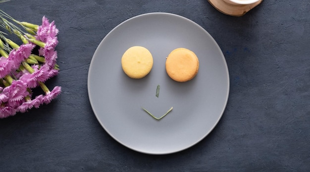 Sourire avec des macarons et des pétales sur une assiette sur une table en pierre sombre avec des fleurs Beau dessert délicieux