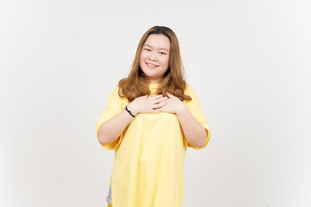 Sourire et main sur la poitrine d'une belle femme asiatique portant un T-shirt jaune isolé sur fond blanc