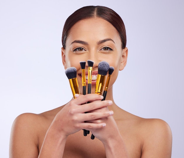 Sourire de maquillage ou portrait de femme avec des pinceaux en studio avec des cosmétiques pour le visage ou des outils de soin de la peau Application de toilettage de visage de beauté ou modèle de fille heureuse isolé sur fond blanc avec maquette