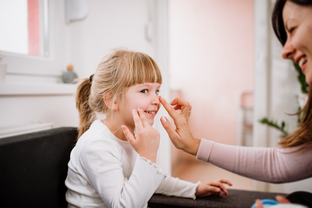 Sourire mère appliquant la crème sur le visage de sa petite fille.