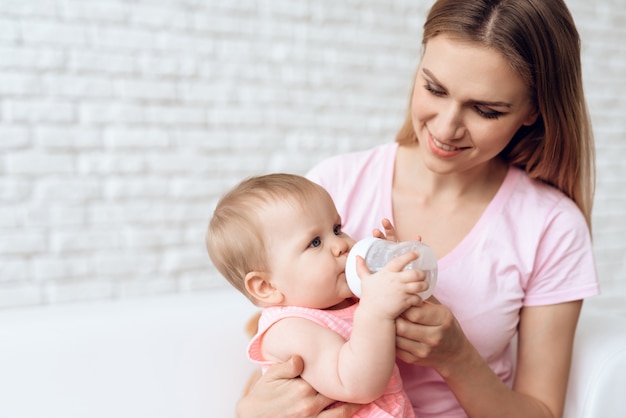 Sourire mère nourrir bébé bouteille de lait à la maison.