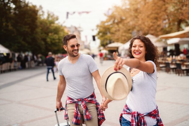 Sourire mignon couple mature, main dans la main et marcher dans la rue au printemps. Femme, pointage, doigt, quoique, homme, porter, bagage