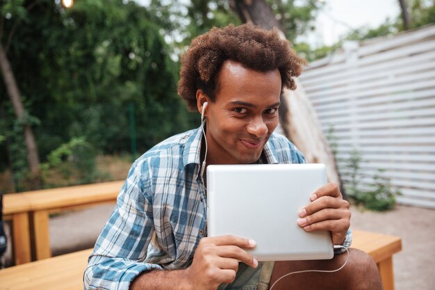 Sourire mignon jeune homme avec tablette, écouter de la musique dans le parc