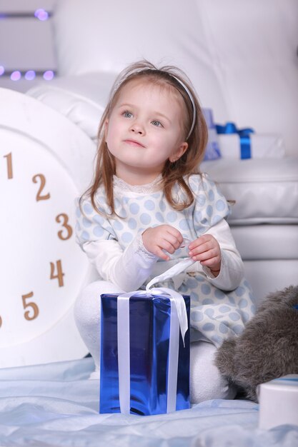 Sourire mignonne petite fille tenant son cadeau de Noël. grande horloge blanche et ours en peluche sur le mur. Célébration du nouvel an.