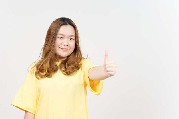 Sourire et montrer les pouces vers le haut de la belle femme asiatique portant un t-shirt jaune isolé sur blanc