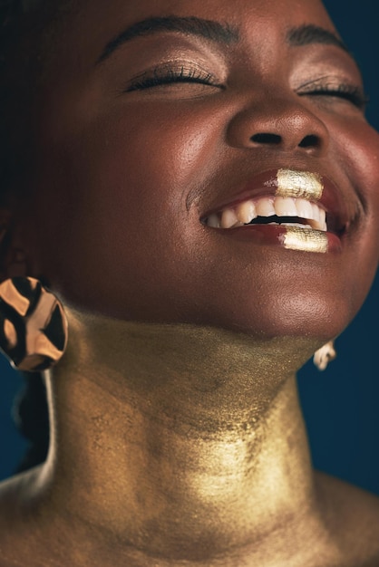 Sourire d'or et maquillage avec le visage d'une femme noire en studio pour le luxe créatif et les cosmétiques Glow glamour art et beauté avec modèle sur fond sombre pour des soins de la peau élégants et un traitement en salon