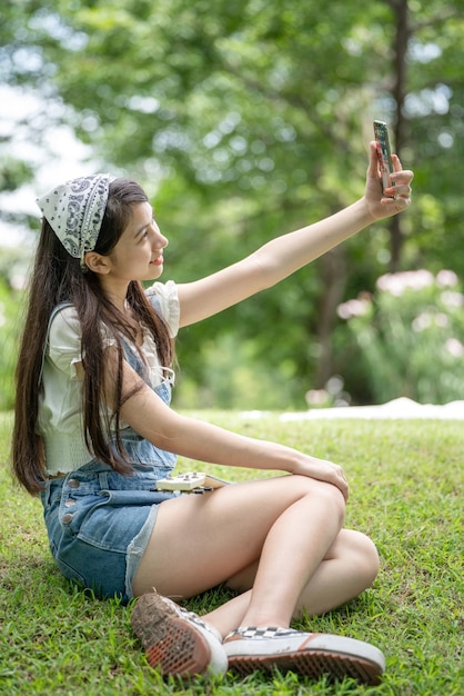 Sourire pensif femme dans le parc à l'aide de téléphone intelligent pour selfie photo Portrait d'une jeune charmante