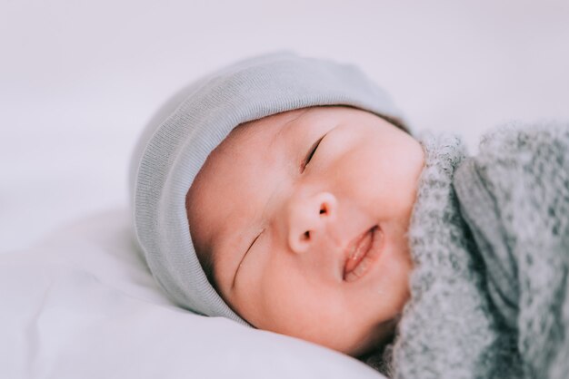 Sourire de petit garçon allongé sur un lit blanc, matin en famille à la maison, hygiène des enfants.