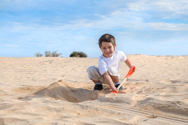 Sourire de petit garçon en t-shirt blanc creuse du sable sur une plage