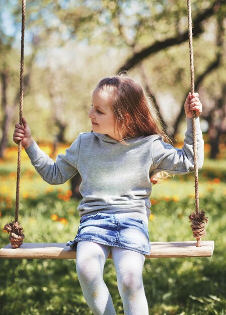 Sourire de petite fille assise sur une balançoire dans le jardin
