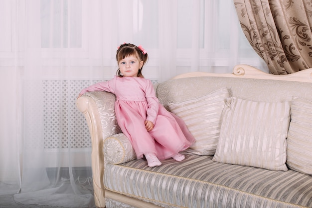 Sourire de petite fille sur le canapé en robe rose à la maison. Concept de l'enfance