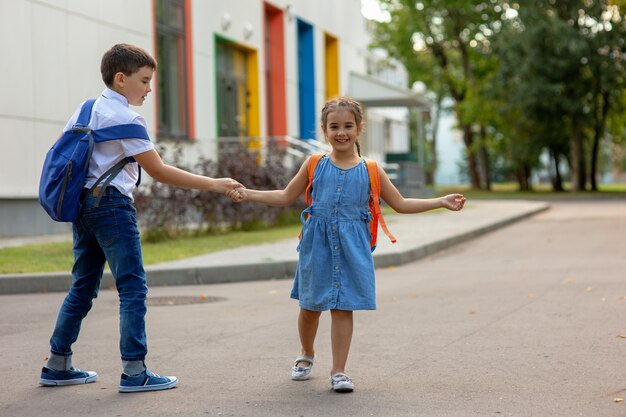 Sourire de petite fille et frère avec des sacs à dos se tiennent la main