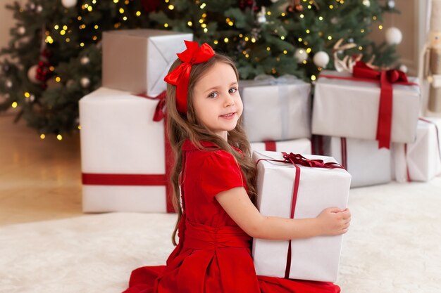 Sourire de petite fille près de sapin de Noël avec des cadeaux