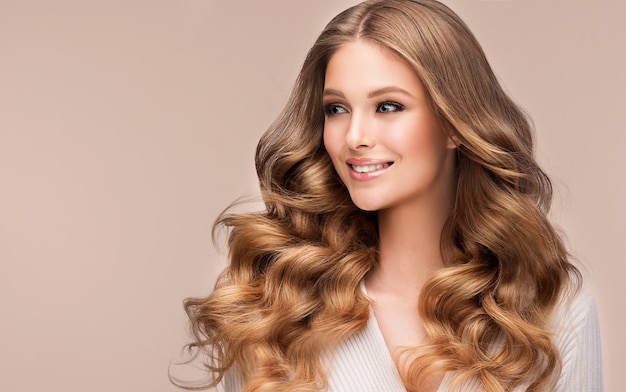 Sourire à pleines dents sur le visage d'un beau modèle avec une longue coiffure blonde profonde ondulée luxuriante Art de la coiffure