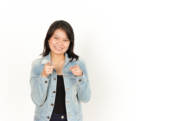 Sourire et pointant vers vous d'une femme asiatique portant une veste en jean et une chemise noire isolée sur blanc