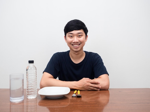 Sourire positif jeune homme assis à table avec vaisselle et couverts avec fond blanc de l'eau