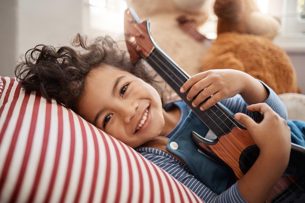 Un sourire qui fait fleurir les roses Portrait d'un adorable jeune garçon jouant avec une guitare dans sa chambre à la maison