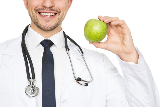 Sourire sain. Coup de gros plan recadrée d'un médecin de sexe masculin souriant joyeusement tenant une pomme isolé sur blanc