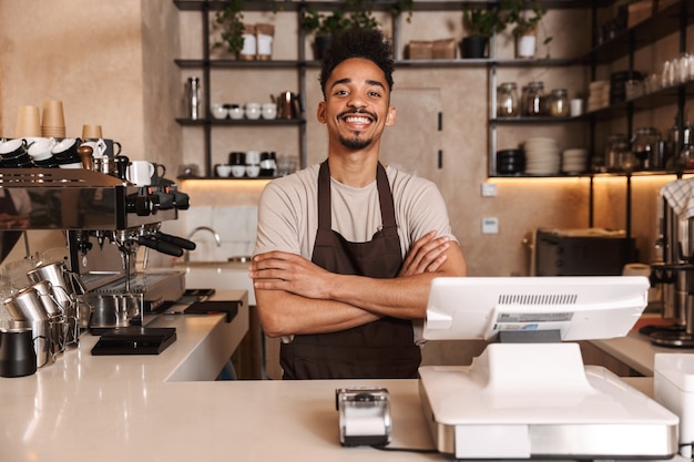 Sourire séduisant homme africain barista debout derrière le comptoir du café