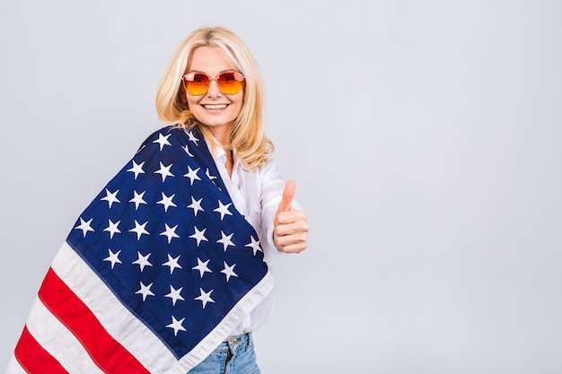 Sourire senior belle femme patriotique portant le drapeau des États-Unis isolé sur fond blanc avec un visage surprise.