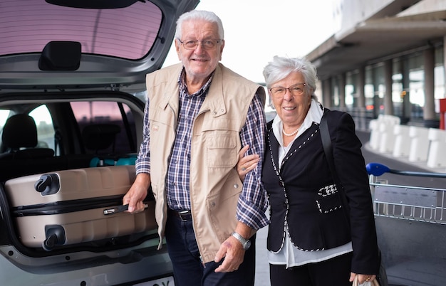 Sourire senior couple de passagers aux cheveux blancs avec chariot et valises à l'aéroport