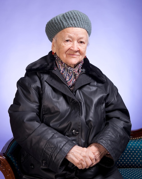 Sourire vieille femme assise sur une chaise sur un fond lilas