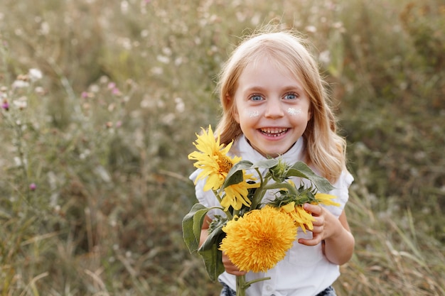 Sourit une fille de 5 ans avec des fleurs jaune vif sur fond d'été